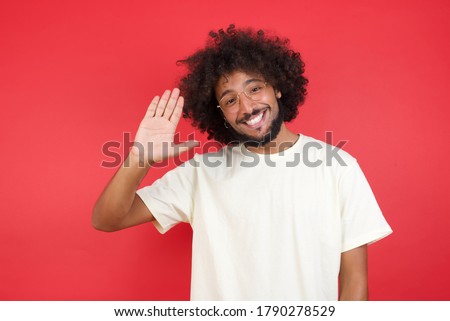 Portrait of cheerful, outgoing friendly-looking young man wearing casual clothes raise one hand and wave, saying hi or hello and smiling with carefree expression as make goodbye or welcome gesture.