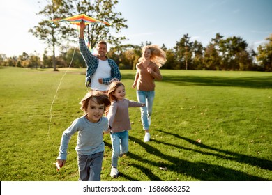 Portrait of cheerful parents with two kids running with kite in the park on a sunny day. Family, kids and nature concept. Horizontal shot. - Powered by Shutterstock