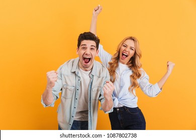 Portrait of cheerful people man and woman in basic clothing smiling and clenching fists like winners or happy people isolated over yellow background - Powered by Shutterstock