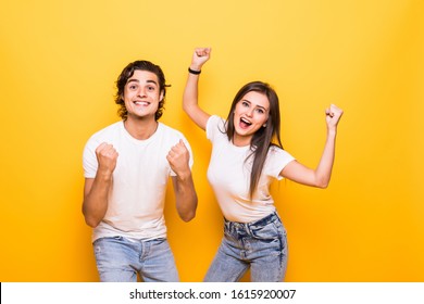 Portrait of cheerful people man and woman in basic clothing smiling and clenching fists like winners or happy people over yellow background - Shutterstock ID 1615920007