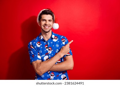 Portrait of cheerful person dressed santa hat blue shirt arms crossed directing empty space isolated on vibrant red color background - Powered by Shutterstock