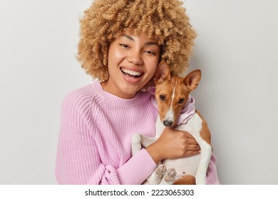 Portrait of cheerful pet owner smiles broadly shows white teeth embraces pedigree dog expresses love takes care of domestic animal wears knitted jumper isolated over grey background. Friendship - Shutterstock ID 2223065303