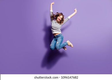 Portrait of cheerful positive girl jumping in the air with raised fists looking at camera isolated on violet background. Life people energy concept