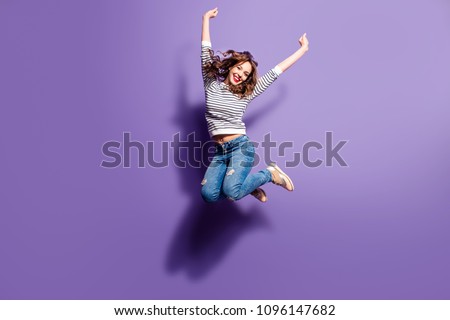 Portrait of cheerful positive girl jumping in the air with raised fists looking at camera isolated on violet background. Life people energy concept
