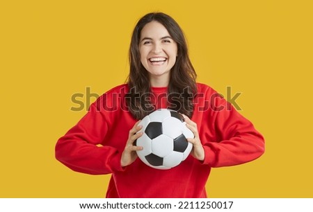 Portrait of cheerful positive young woman who is having fun catching soccer ball thrown to her. Young woman with traditional black and white soccer ball in hands laughing isolated on orange background