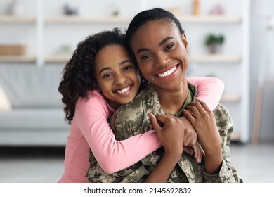 Portrait Of Cheerful Pretty Curly Black Teen Girl Hugging Her Mom Soldier From Behind And Smiling At Camera, Young Black Woman In Military Uniform Return Home From Army, Cuddling With Her Daughter