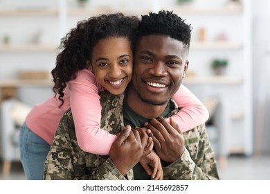 Portrait Of Cheerful Pretty Curly Black Teen Girl Hugging Her Dad Soldier From Behind And Smiling At Camera, Young Black Man In Military Uniform Return Home From Army, Cuddling With His Daughter