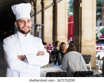 Portrait Of Cheerful Professional Chef On Background With Restaurant Guests