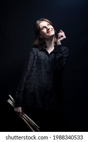 Portrait Of A Cheerful Rock N Roll Drumming Girl Holding Sticks In Her Hands. Musician In Black. On A Dark Background Happy Drummer Woman With Drum Sticks