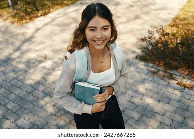 Portrait of cheerful schoolgirl holding books and looking up at camera - Powered by Shutterstock