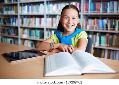 Portrait of cheerful schoolgirl looking at camera while sitting in library - Powered by Shutterstock