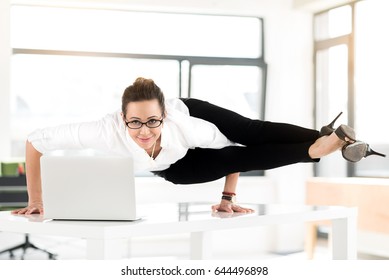 Portrait of cheerful secretary in yoga posture having job in comfortable office. She watching at camera while standing on hands on desk