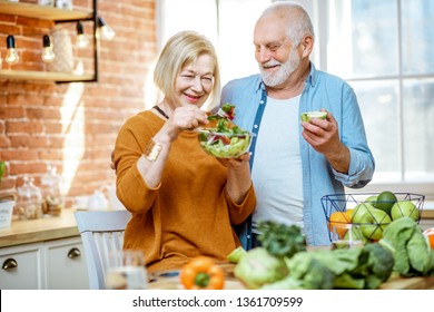 Portrait Of A Cheerful Senior Couple With Salad And Healthy Food On The Kitchen At Home. Concept Of Healthy Nutrition In Older Age