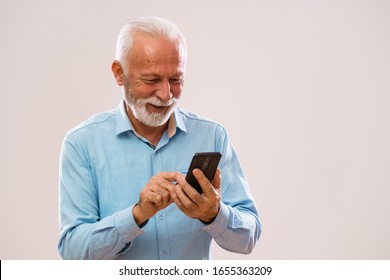 Portrait of cheerful senior man who is using smartphone.
