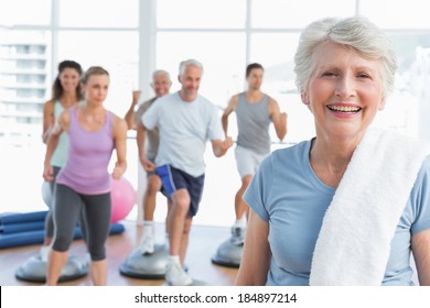 Portrait of a cheerful senior woman with people exercising in the background at fitness studio - Powered by Shutterstock