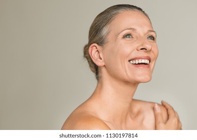Portrait of a cheerful senior woman smiling while looking away isolated on gray background. Happy mature woman after spa massage and anti-aging treatment on face.