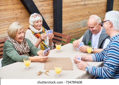 Portrait Of Cheerful Seniors Playing Card Game At Lunch Table On Outdoor Terrace  Laughing Happily