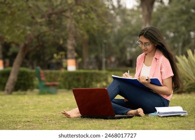 Portrait of a cheerful smart student girl studying at park with books, laptop and notebooks . Indian student educational young teenager girl at park outside campus  - Powered by Shutterstock