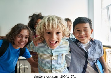 Portrait of cheerful smiling boy with diverse friends schoolmates schoolkids having fun standing posing in classroom looking at camera happy after school reopen. Diversity. Back to school concept.