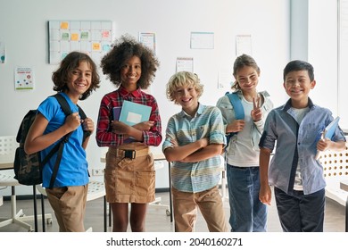 Portrait of cheerful smiling diverse schoolchildren standing posing in classroom holding notebooks and backpacks looking at camera happy after school reopen. Diversity. Back to school concept. - Powered by Shutterstock