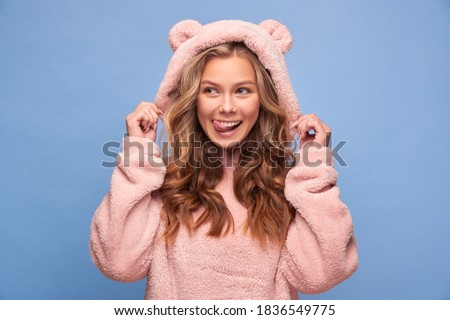 Portrait of a cheerful smiling girl with white teeth in pink bear clothes on a blue background