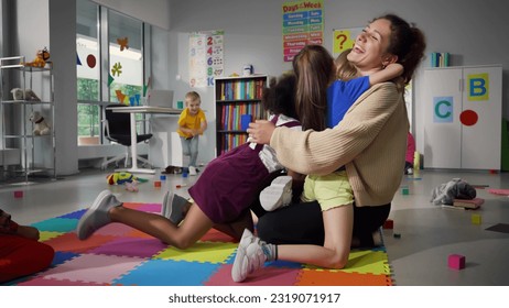 Portrait of cheerful smiling teacher and happy diverse schoolchildren hugging in playroom of kindergarten. Happy preschool kids embrace favorite teacher in nursery school - Powered by Shutterstock