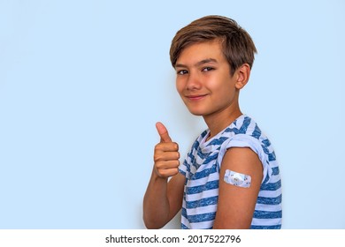  Portrait Of Cheerful Smiling Teen Boy Showing Vaccinated Arm With Sticking Patch On The Shoulder After Getting Shot And Thumb Up. Effective Covid Vaccine Against New Delta Variant In Young People.