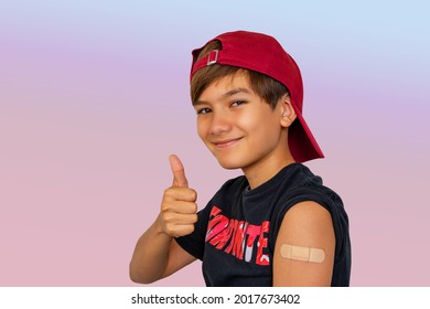 Portrait Of Cheerful Smiling Teen Boy Showing Vaccinated Arm With Sticking Patch On The Shoulder After Getting Shot And Thumb Up. Effective Covid Vaccine Against New Delta Variant In Young People.