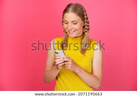 Portrait of a cheerful smiling young girl in yellow clothes standing isolated over pink background and using mobile phone