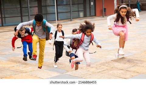 Portrait Of Cheerful Tween Boys And Girls With School Backpacks Running In Schoolyard In Spring Day.