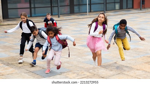 Portrait Of Cheerful Tween Boys And Girls With School Backpacks Running In Schoolyard In Spring Day.