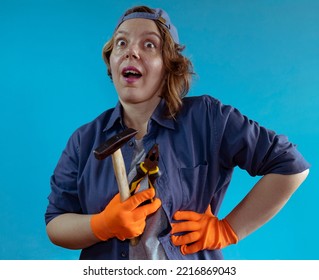 Portrait Of A Cheerful Woman In A Cap And Shirt Holds A Hammer And Pliers In Her Hands On A Blue Isolated Background. Cheerful Female Plumber. Woman Work