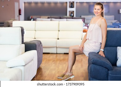 Portrait of cheerful woman consumer choosing sofa in furniture shop