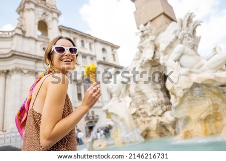 Portrait of a cheerful woman eating ice cream in cone while visiting famous Navona square near fountain in Rome. Concept of happy summer vacations, traveling famous italian landmarks
