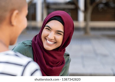 Portrait Of Cheerful Woman In Hijab Smiling While Talking To Bald Friend. Best Friends On Street Laughing. Back View Of Beautiful Islamic Woman With Toothy Smile Looking At Friend Outdoor.