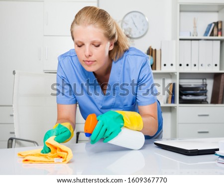 Portrait of cheerful woman janitor in latex gloves cleaning workplace in office 