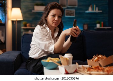 Portrait Of Cheerful Woman Sitting On Couch Smiling At Camera While Enjoying Home-delivered Late At Night In Living Room. Caucasian Female Holding Beer Bottle. Takeaway Food Delivery