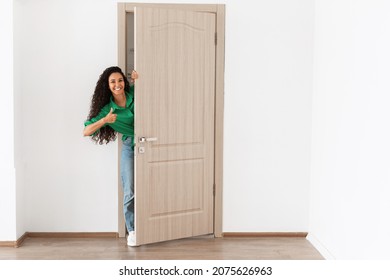 Portrait of cheerful woman standing in doorway of modern apartment, millennial female homeowner holding door looking out and smiling, greeting visitor, showing thumbs up like sign gesture, approving - Powered by Shutterstock