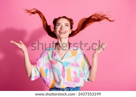 Portrait of cheerful woman wear print shirt hands fluttering foxy hair look up at logo empty space isolated on pink color background