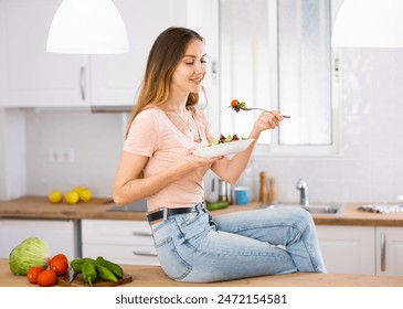 Portrait of cheerful young adult woman eating vegetable salad in home kitchen - Powered by Shutterstock