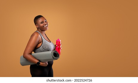 Portrait Of Cheerful Young African American Lady In Sportswear Holding Fitness Mat And Bottle With Water, Getting Ready For Training Or Sport Workout, Posing At Brown Studio, Free Copy Space, Panorama