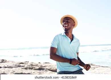 Portrait of cheerful young african man with hat enjoying at the beach on summer day