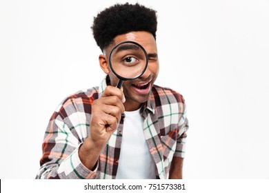 Portrait of a cheerful young african man looking through magnifying glass isolated over white background