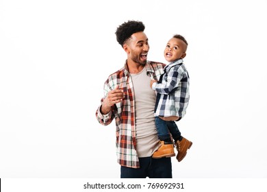 Portrait of a cheerful young african man holding his little son while standing and laughing isolated over white background