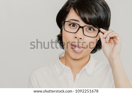 Portrait of cheerful young Asian businesswoman wearing eyeglasses looking at camera and showing tongue