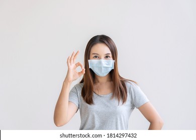 Portrait Of Cheerful Young Asian Girl With Protective Face Mask Showing Fine In Sign Language Hand And Smiling At Camera On White Background. Copy Space