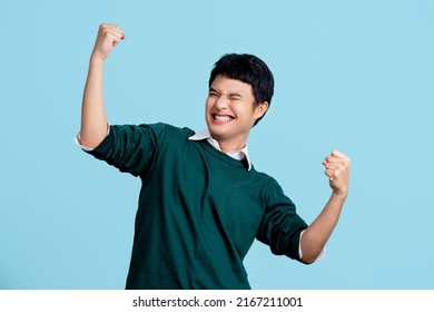 Portrait of a cheerful young Asian man in casual clothes. He raised his fist with a happy smile on his face as a gesture of celebration.