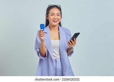 Portrait Of Cheerful Young Asian Woman Holding Banking Token And Holding Smartphone Isolated On White Background. Concept Money Transfer Via Internet