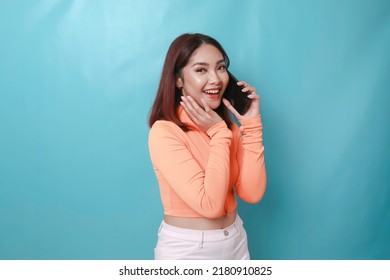 A Portrait Of A Cheerful Young Asian Woman Having A Phone Call, Isolated On Blue Background