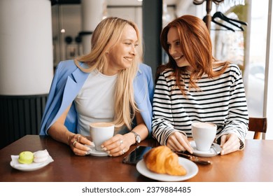 Portrait of cheerful young best girlfriends sitting at modern cafe, communicating and sharing stories, spending relax in coffee shop. Two women friends sitting in cafeteria and talking. - Powered by Shutterstock